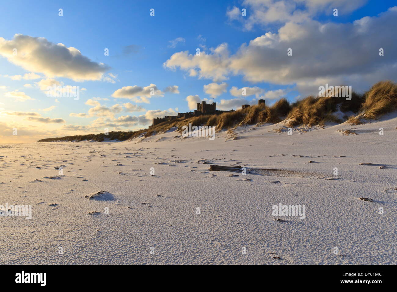 Fresh Spring snow at dawn highlight ripples and marks in the sand beneath Bamburgh Castle,  Bamburgh, Northumberland, England Stock Photo