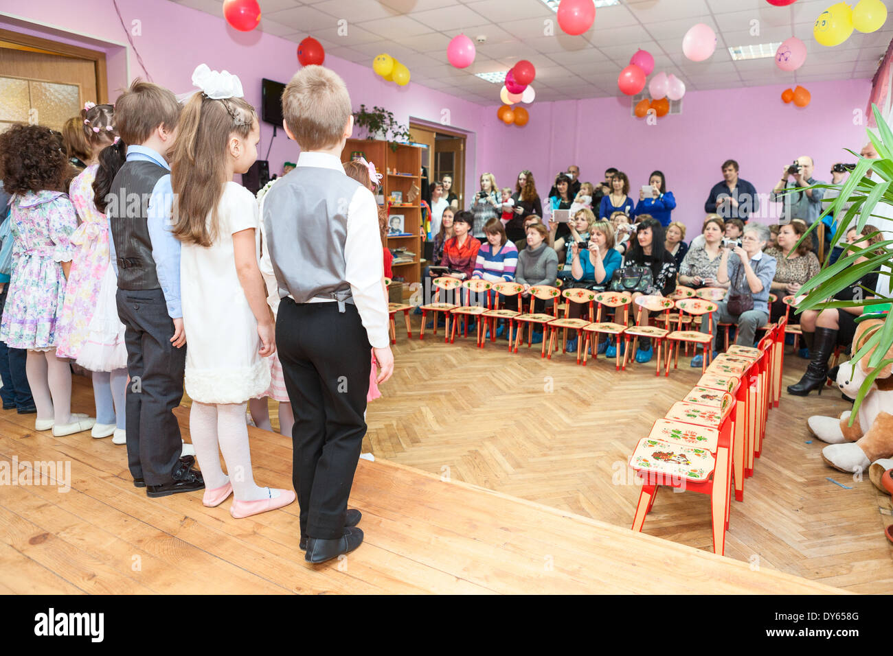 Boys and girls sing a song on theater stage in kindergarten, Russia. Graduation party is in daycare center Stock Photo