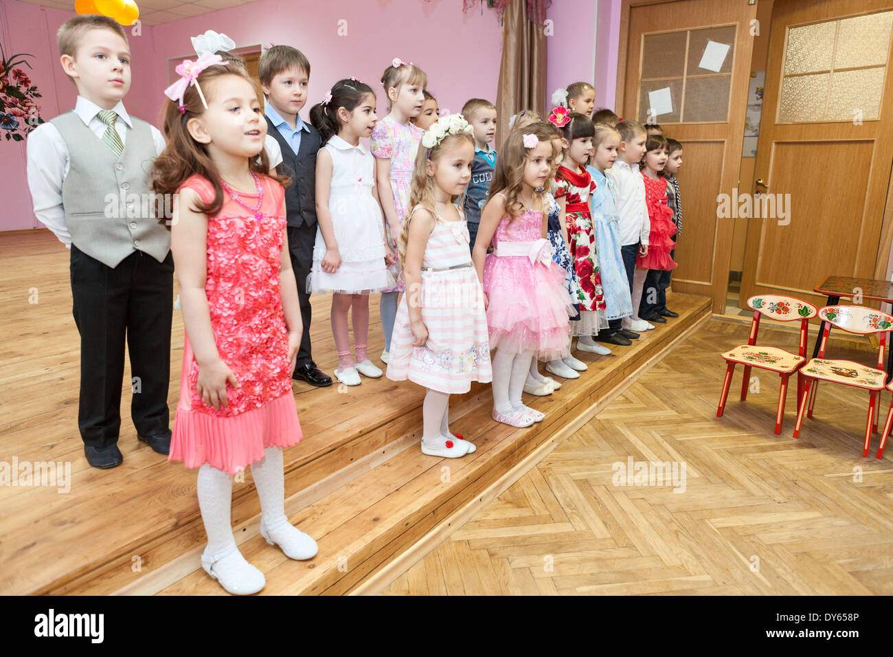 Boys and girls sing a song on theater stage in kindergarten, Russia. Graduation party is in daycare center Stock Photo