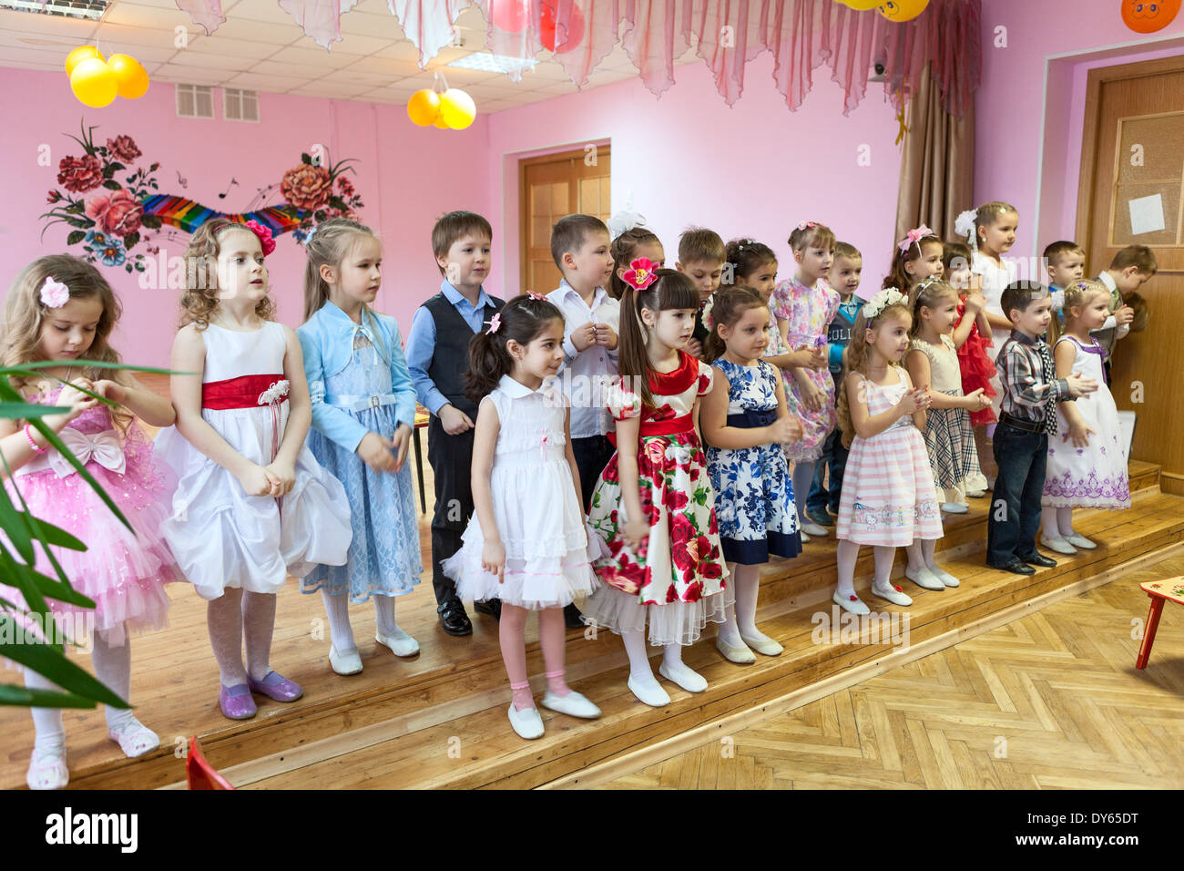 Boys and girls stay on theater stage in kindergarten and sing a song, Russia. Graduation party is in daycare center Stock Photo