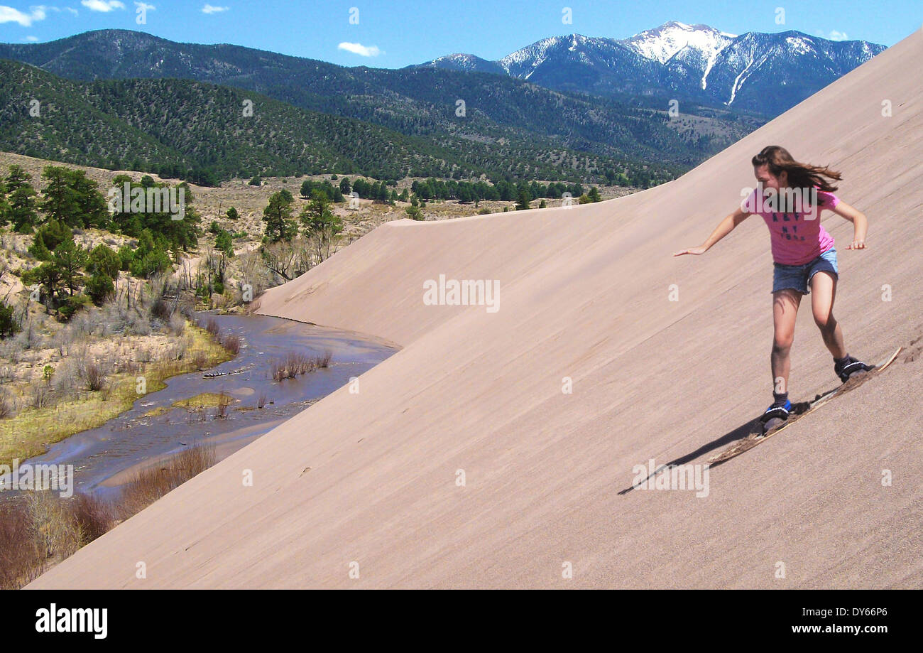 Sandboarder rides down a dune above Medano Creek at the Castle Creek Picnic Area in Great Sand Dunes National Park May 8, 2009 in Mosca, Colorado. Stock Photo