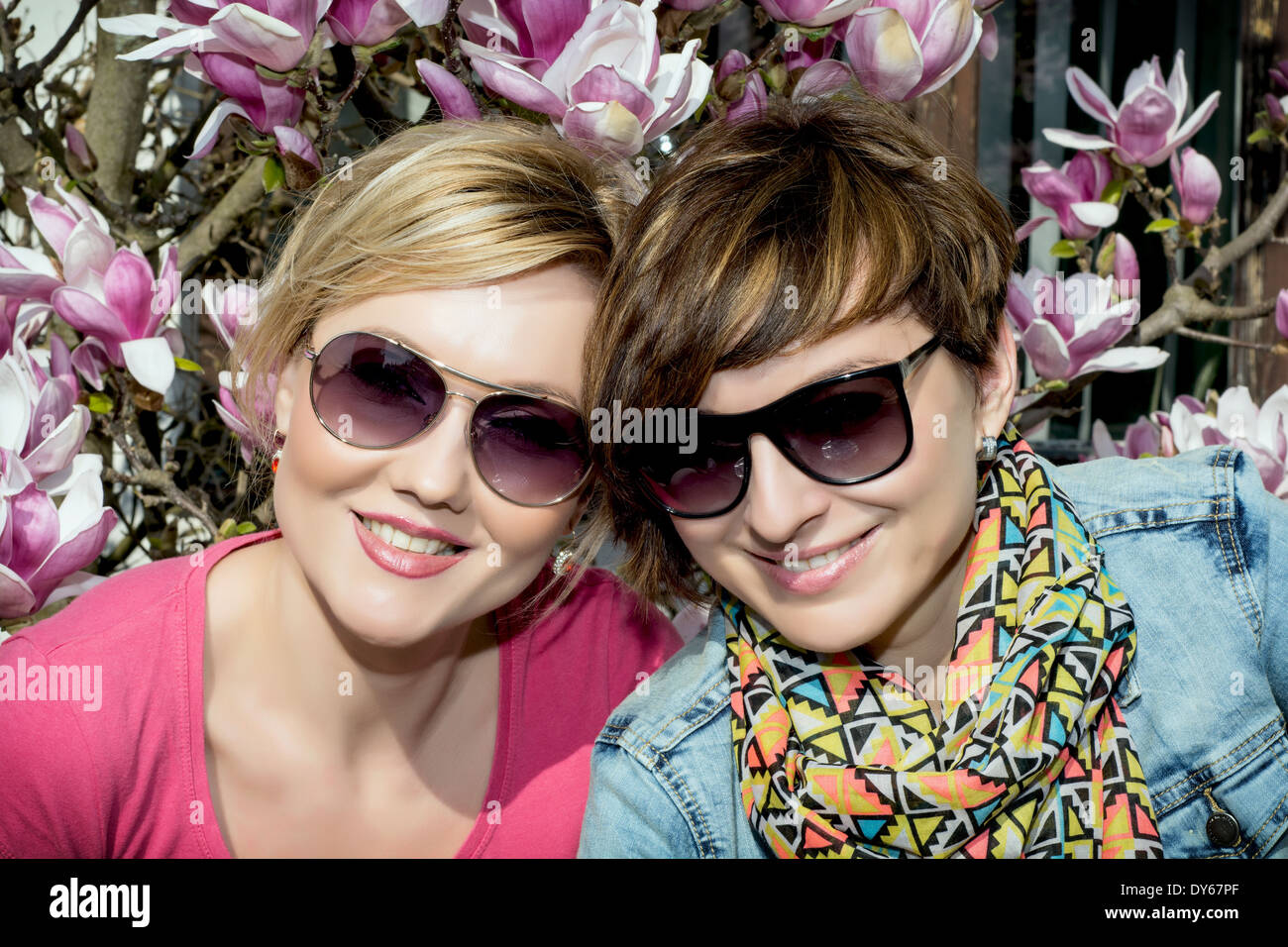 Two young caucasian women posing with blooming magnolia. Women's beauty and fashion. Stock Photo