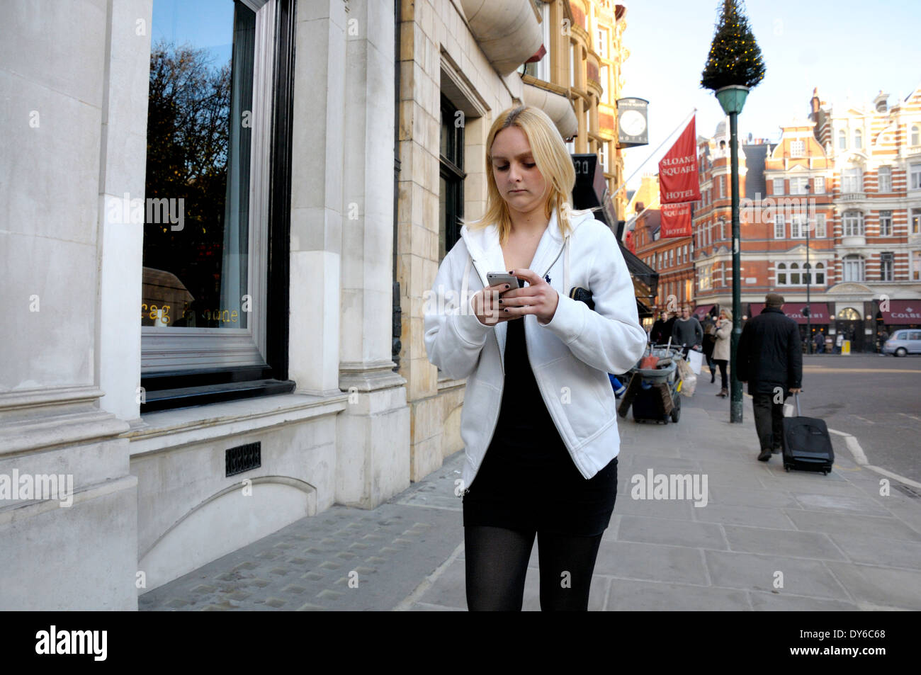 London, England, UK. Young woman walking and using her mobile phone in Sloane Square Stock Photo
