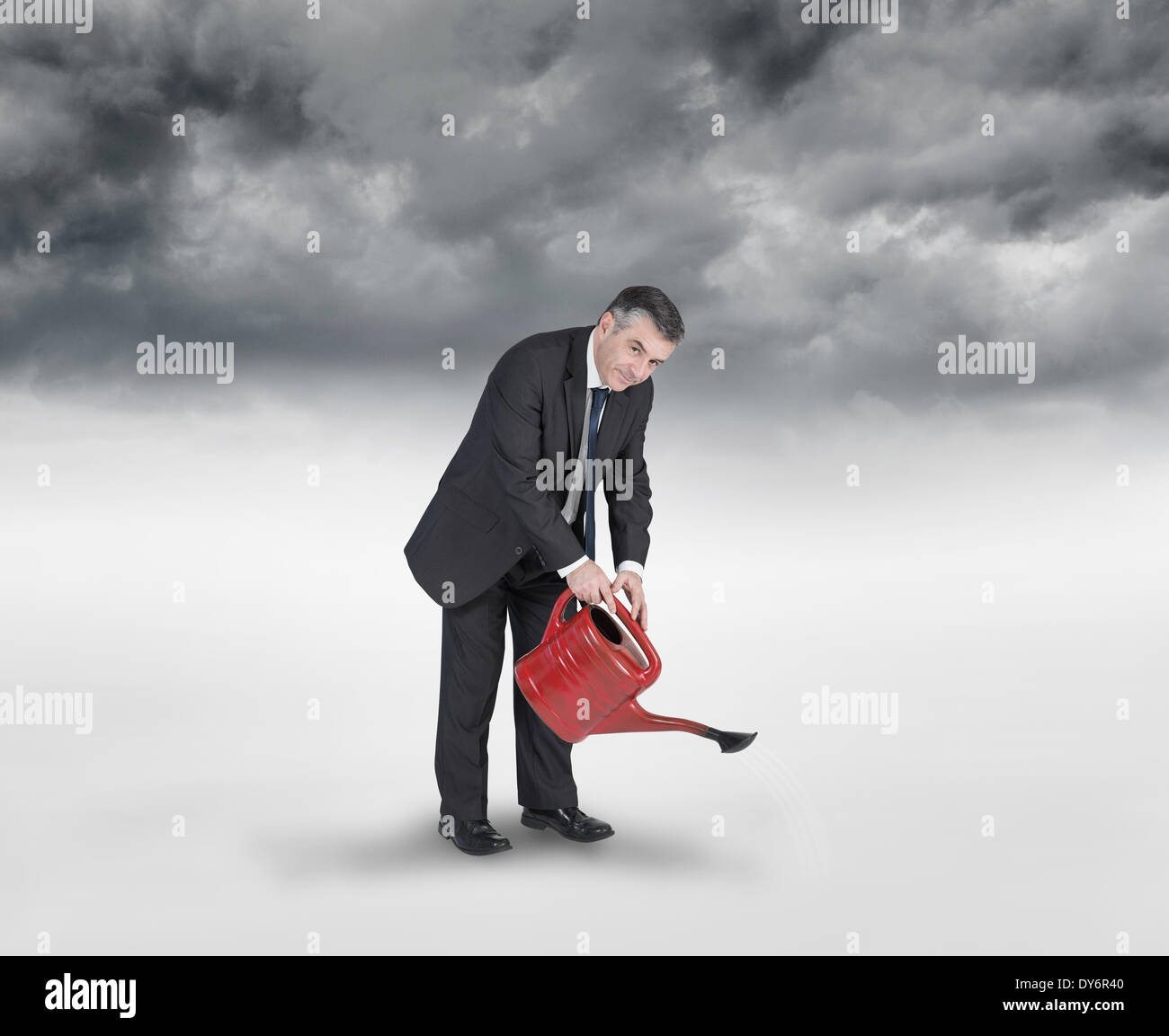 Composite image of mature businessman using watering can Stock Photo
