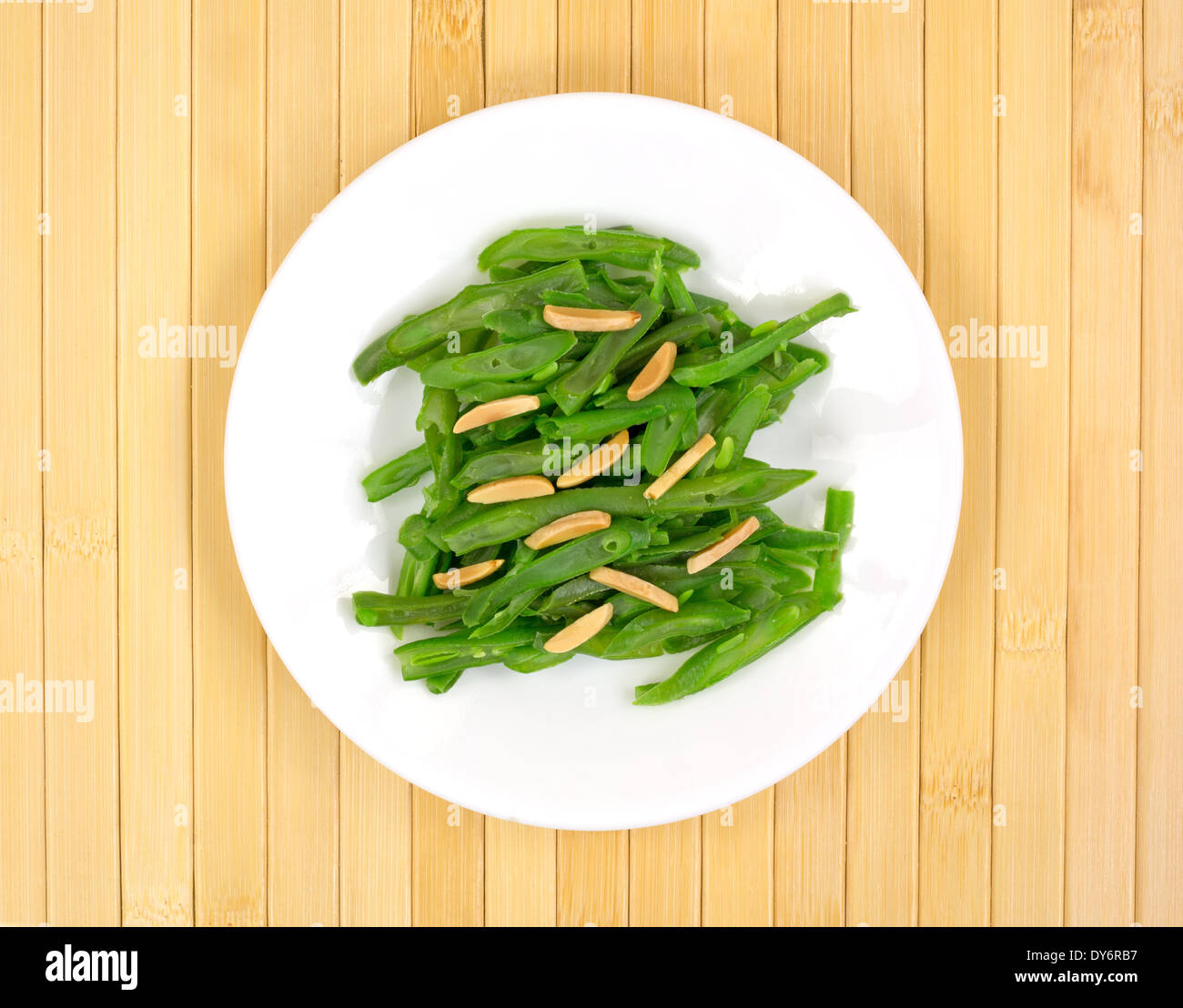A small serving of green beans with sliced almonds on a white plate atop a wood place mat. Stock Photo