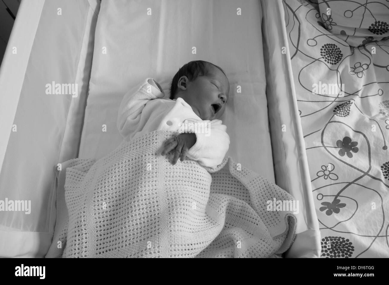 Black and white shot of a three day old newborn baby girl in her crib yawning Stock Photo