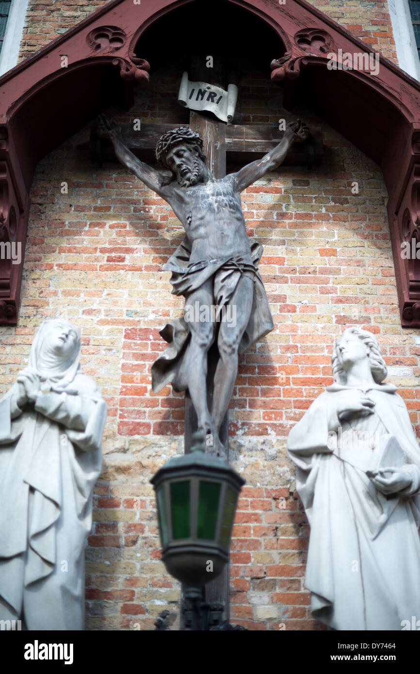 Church Of Our Lady Crucifixion Statue Bruges Belgium // BRUGES, Belgium — A crucifixion statue adorns the exterior of the Church of Our Lady (Onze-Lieve-Vrouwekerk), exemplifying medieval religious sculpture. This architectural detail demonstrates the Gothic tradition of incorporating sacred imagery into church decoration. The sculpture represents the integration of religious art and architecture characteristic of medieval church design. Stock Photo