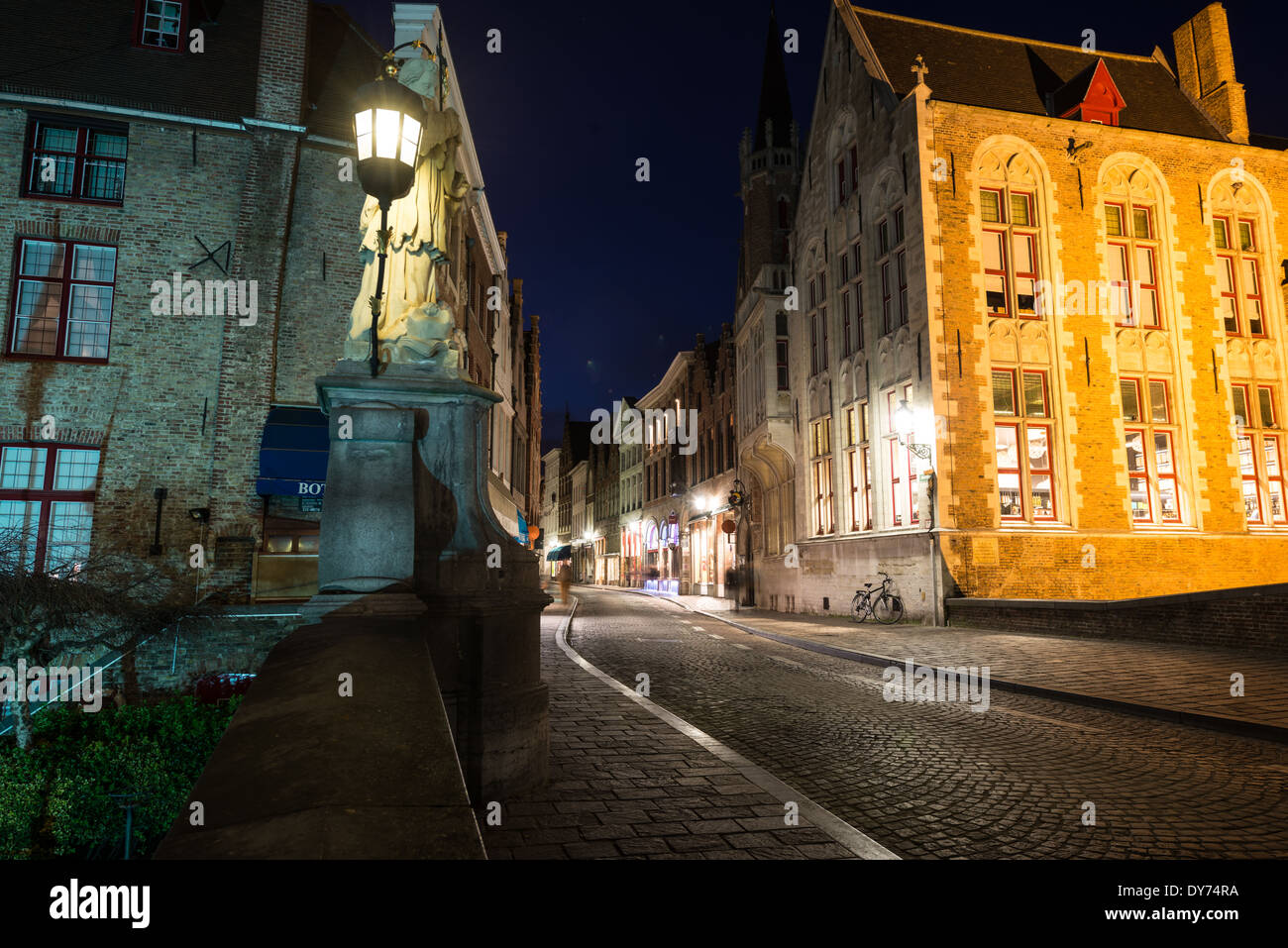 Bruges Historic Center At Night Bruges Belgium // BRUGES, Belgium — A nighttime view from a canal bridge captures the illuminated streets of Bruges' historic center. Traditional lighting reflects off the calm waters, creating a romantic atmosphere characteristic of medieval Bruges after dark. The scene demonstrates how evening illumination enhances the historic character of this UNESCO World Heritage site. Stock Photo