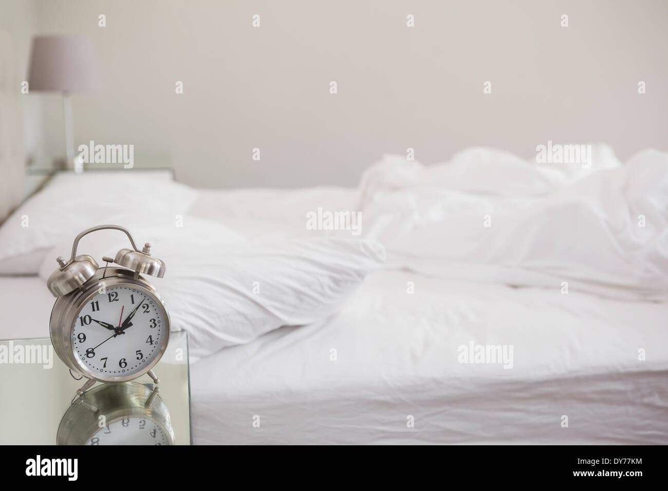 Messy bed with alarm clock on bedside table Stock Photo