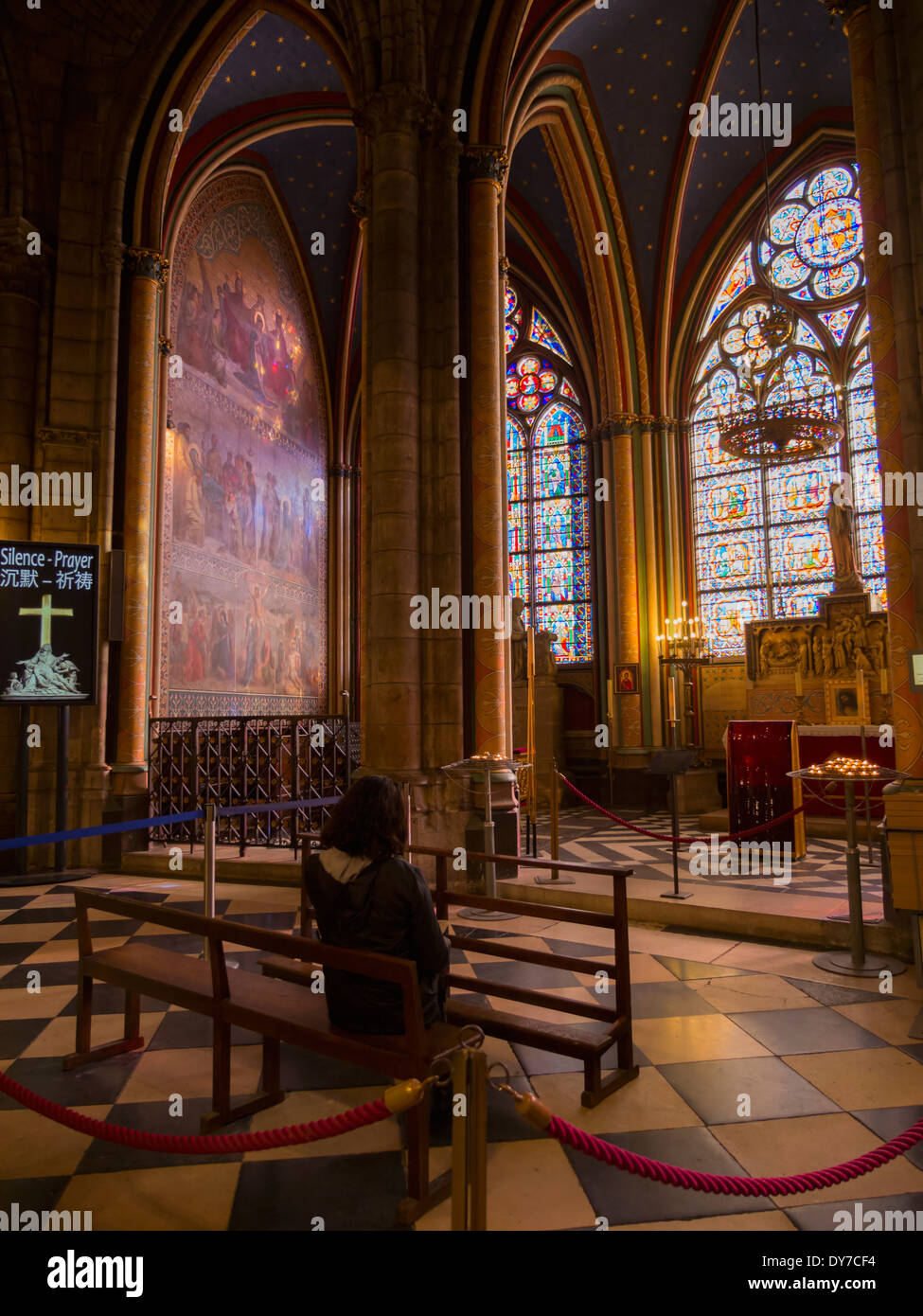 Interior of Notre Dame Cathedral, Paris. A woman prays in a chapel. Stock Photo