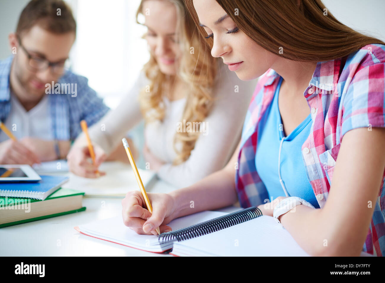 Smart girl and her groupmates on background carrying out written task at lesson Stock Photo