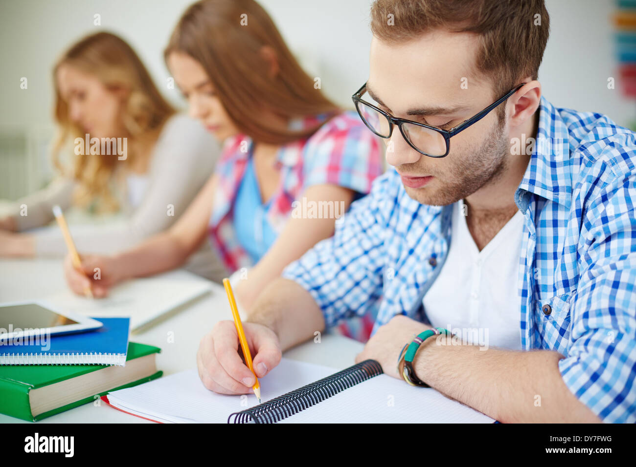 Serious guy and his groupmates on background carrying out written task at lesson Stock Photo
