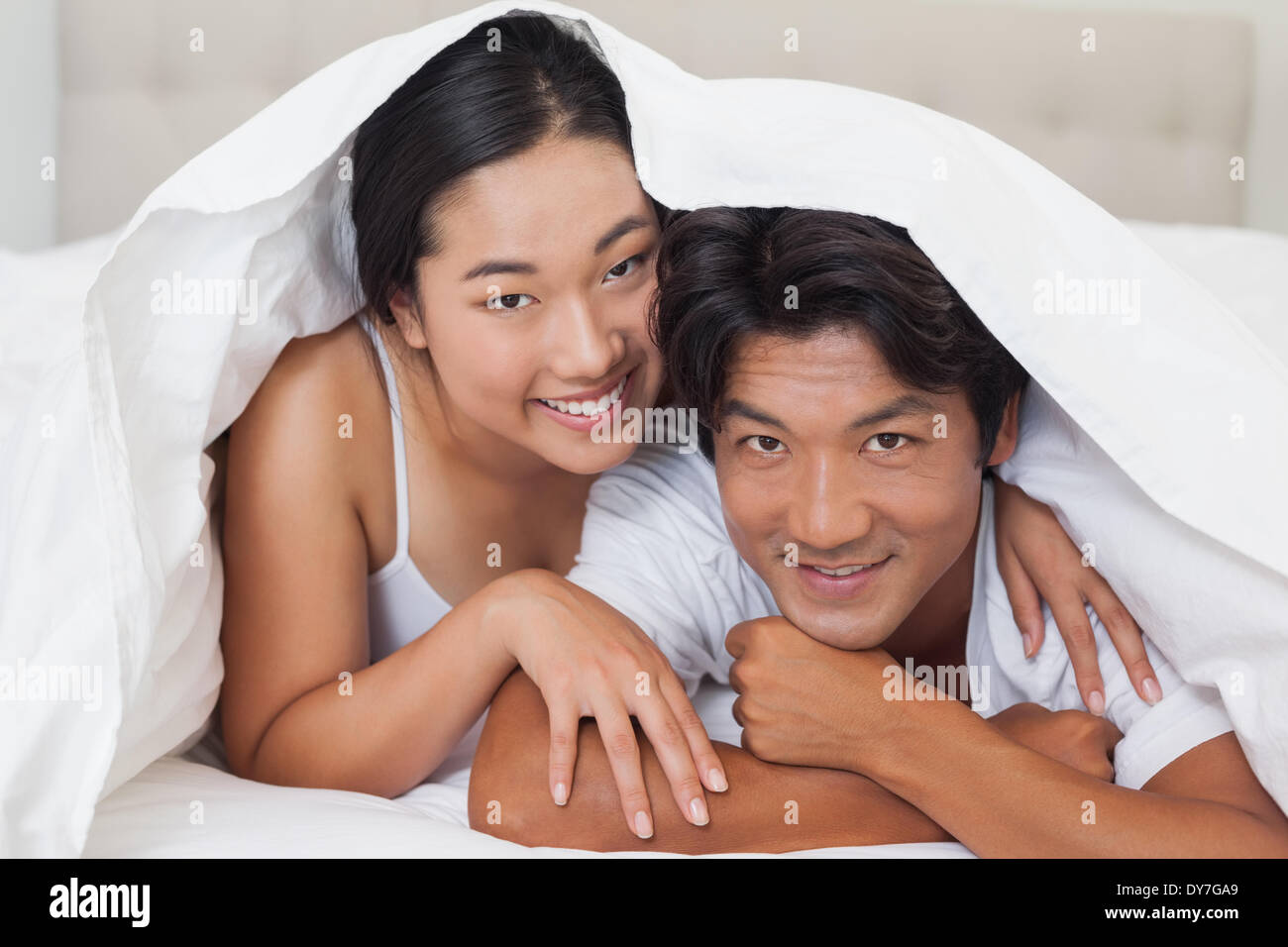 Happy couple lying on bed together under the duvet Stock Photo