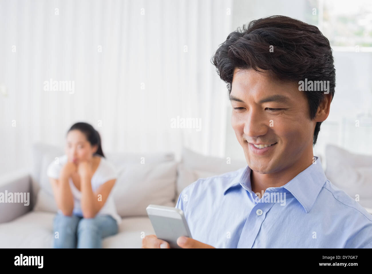 Man sending a text while girlfriend watches from couch Stock Photo