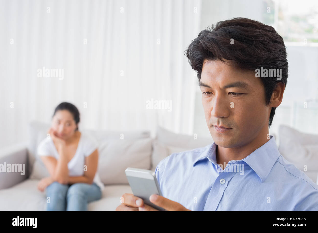 Man sending a text while girlfriend watches from couch Stock Photo