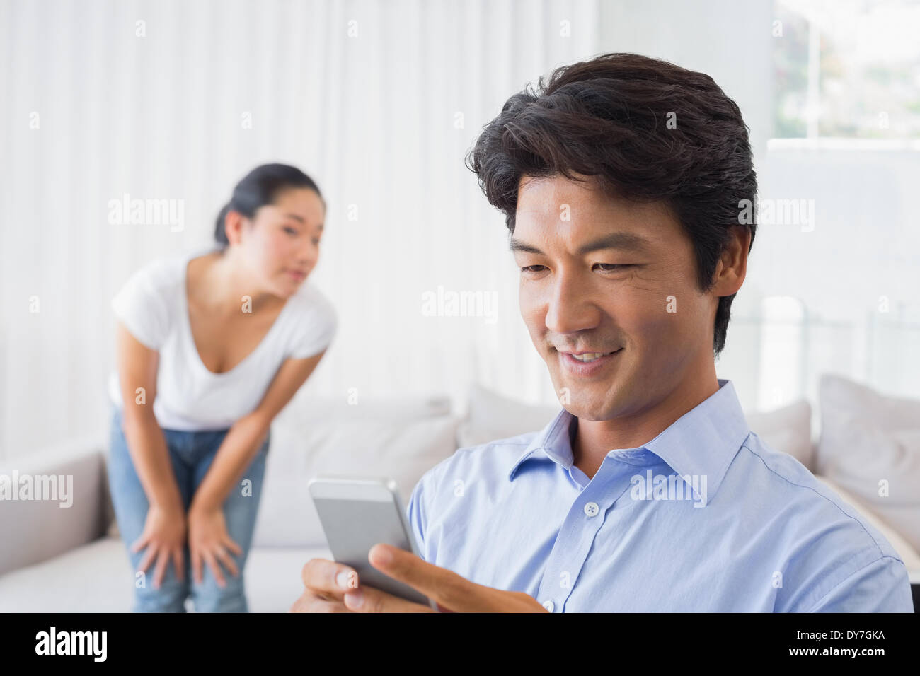 Man sending a text while girlfriend watches from couch Stock Photo