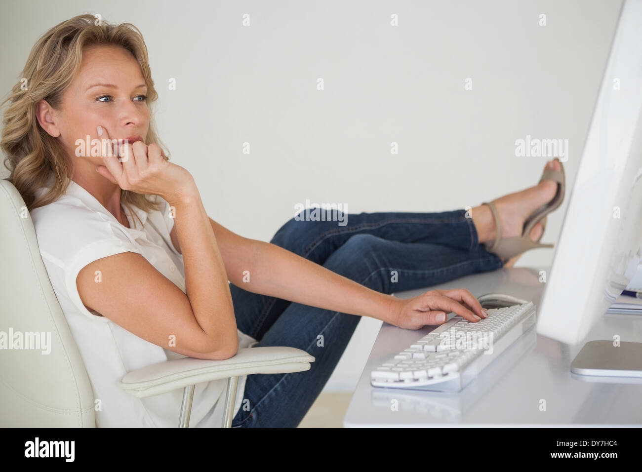 Donna seduta su una scrivania utilizzando un computer, i piedi su un  poggiapiedi, vista laterale Foto stock - Alamy