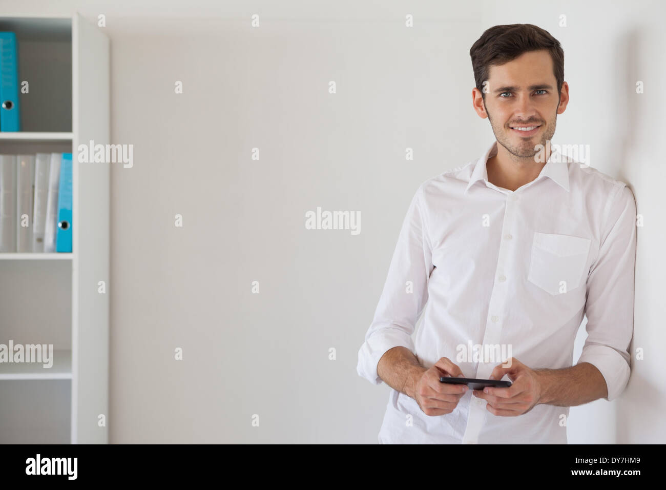Casual businessman leaning against wall sending a text Stock Photo