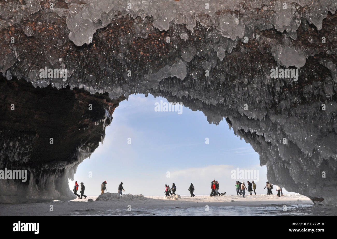 Ice formations and icicles hanging from ceiling in a cave and people walking on frozen Lake Superior, Apostle Islands National Stock Photo