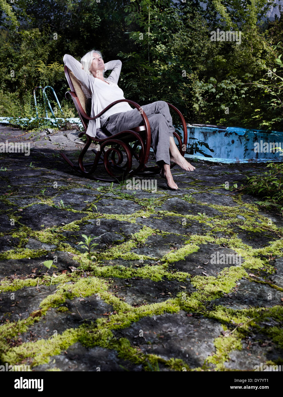 Woman, 65-75 years, sitting in an overgrown garden in a rocking chair, Innsbruck, Tyrol, Austria Stock Photo