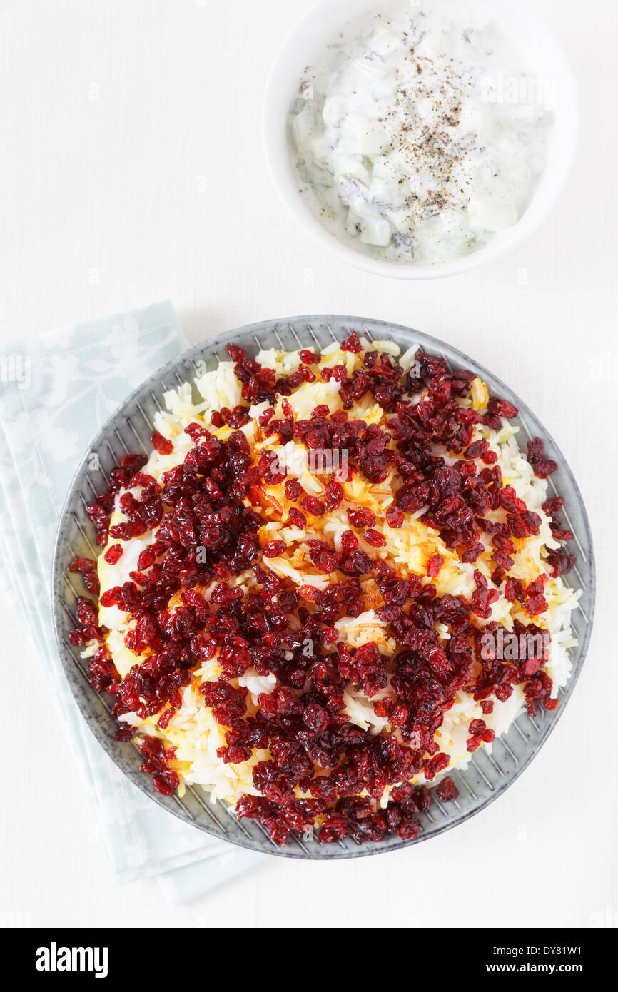 Persian saffron rice with barberries and bowl of mint yoghurt on white