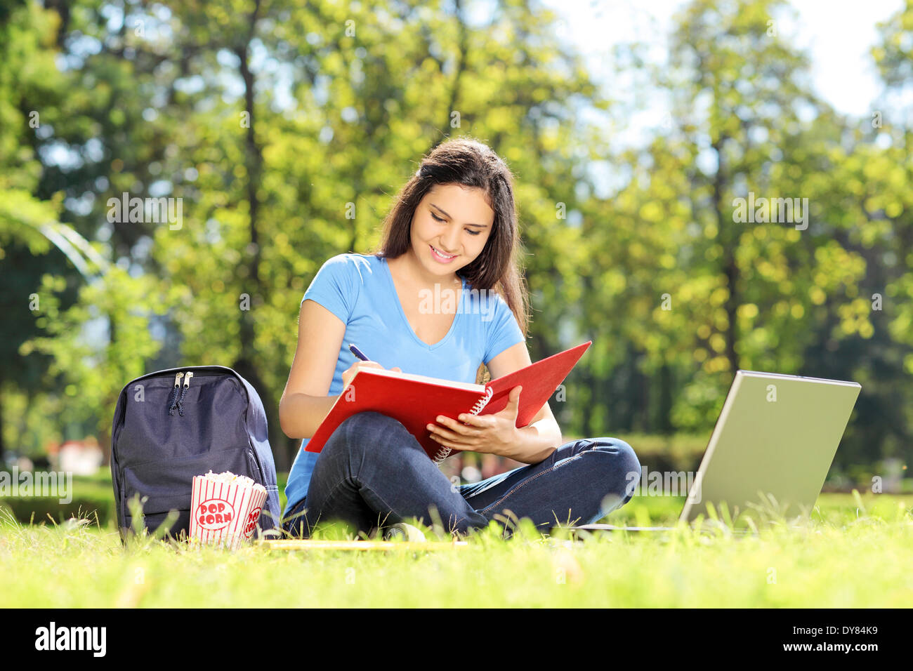 Girl sitting on grass and writing in a notebook outdoors Stock Photo