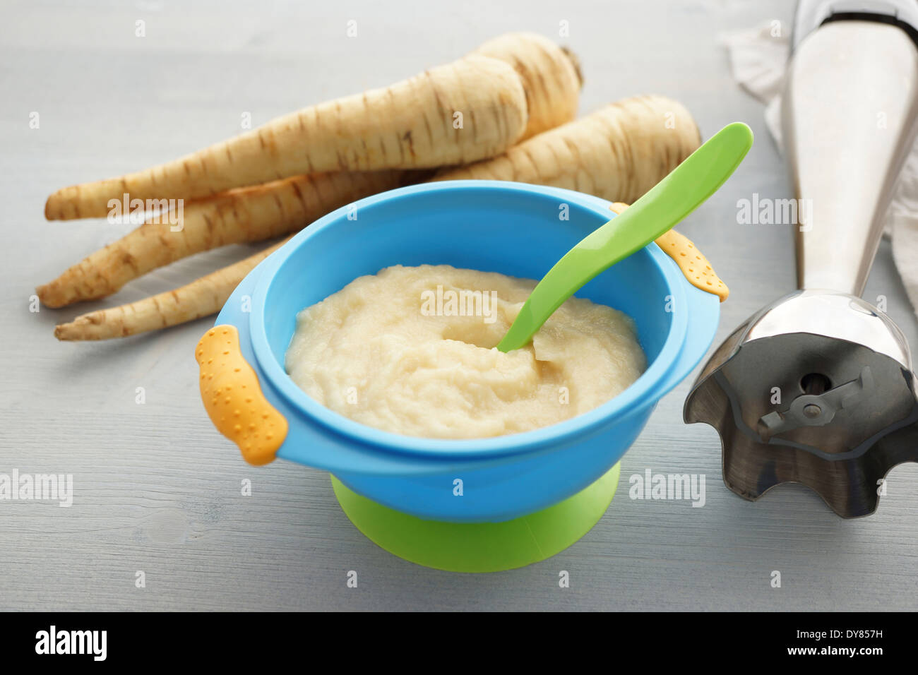 Immersion blender, bowl of parsnip puree and parsnips on wooden table Stock Photo