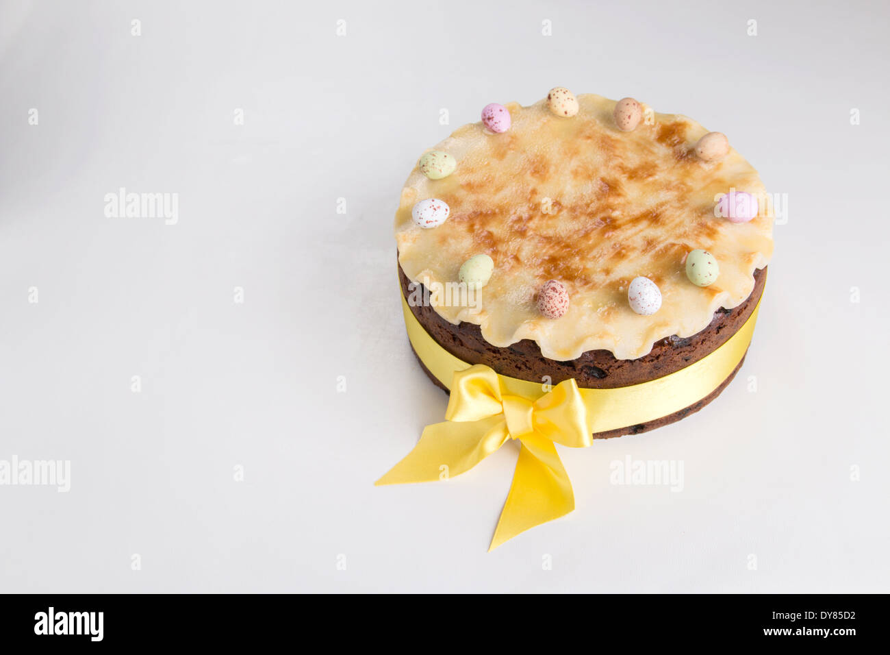 Simnel cake on a light background with fluted marzipan a yellow ribbon with a bow with 11 coloured eggs (31 of 35) Stock Photo