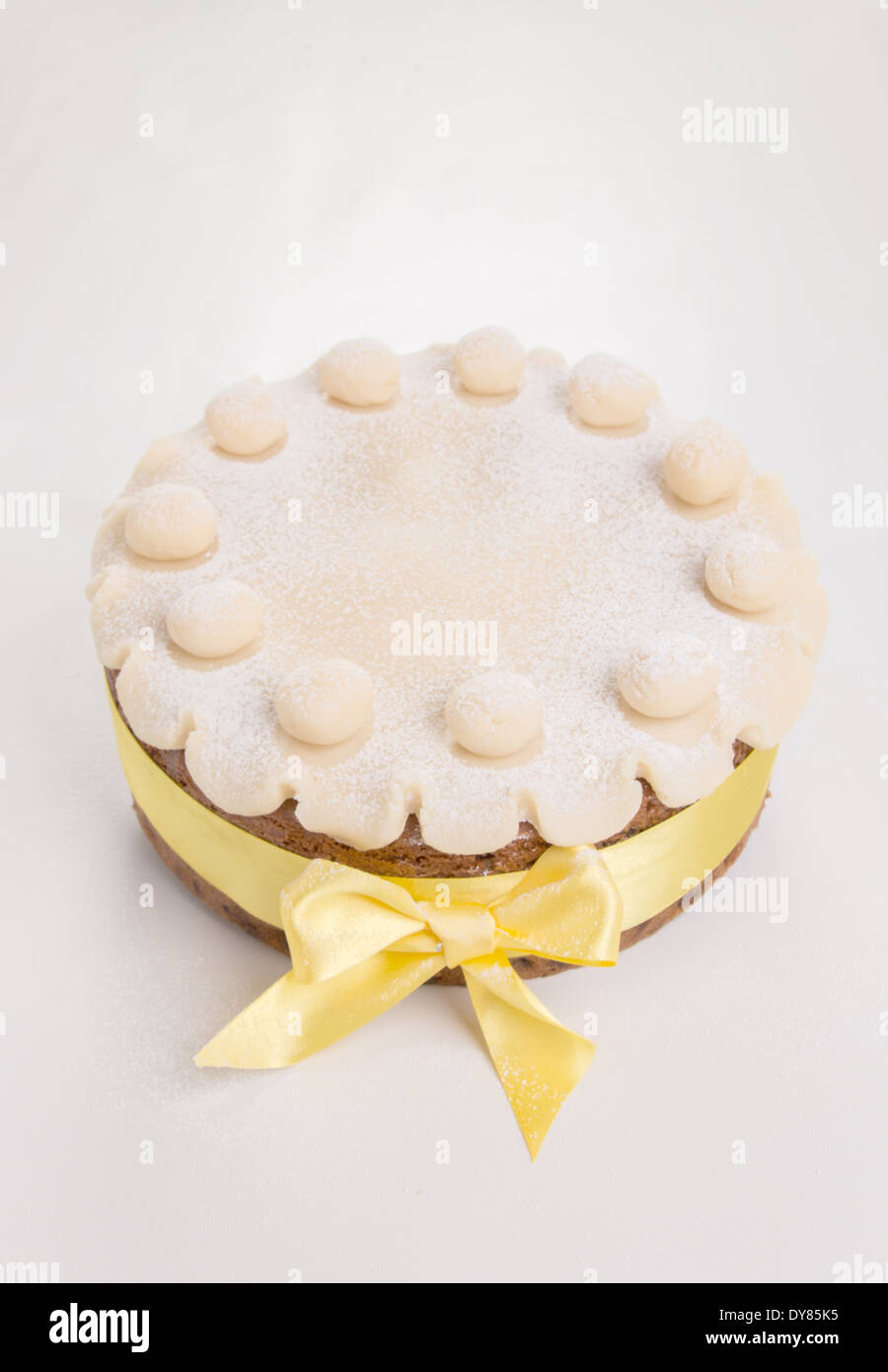 Simnel cake with basic marzipan decoration with a yellow ribbon sprinkled with icing sugar/powdered sugar,portrait (17 of 35) Stock Photo