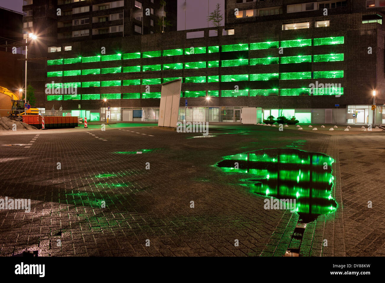 Urban abstract, green lights of a multi storey car park with reflections on water after the rain at night . Stock Photo