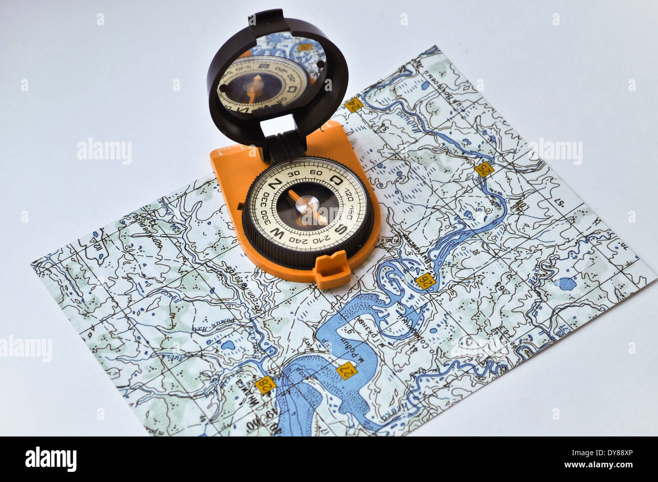 Topographic map lies on a white background, and there is a magnetic compass in a black case on an orange ground. Stock Photo