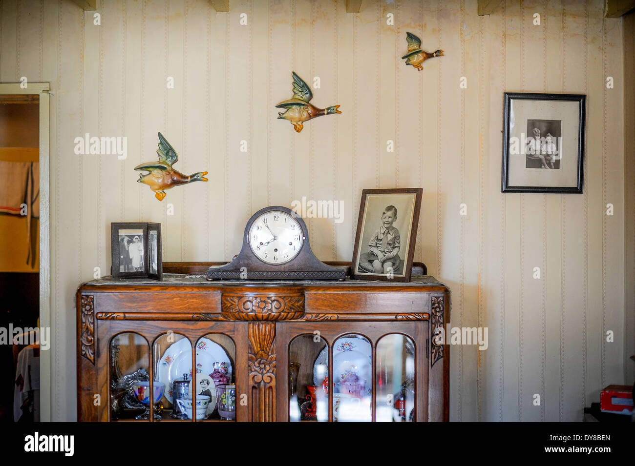 Flying ducks on vintage wallpaper in a second world war living room. Old sideboard, clock and framed photographs Stock Photo