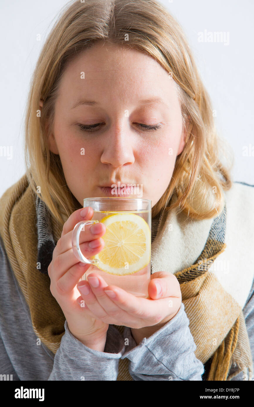 Young woman lying in bed, has a cold, fever, flu, drinking a hot lemon