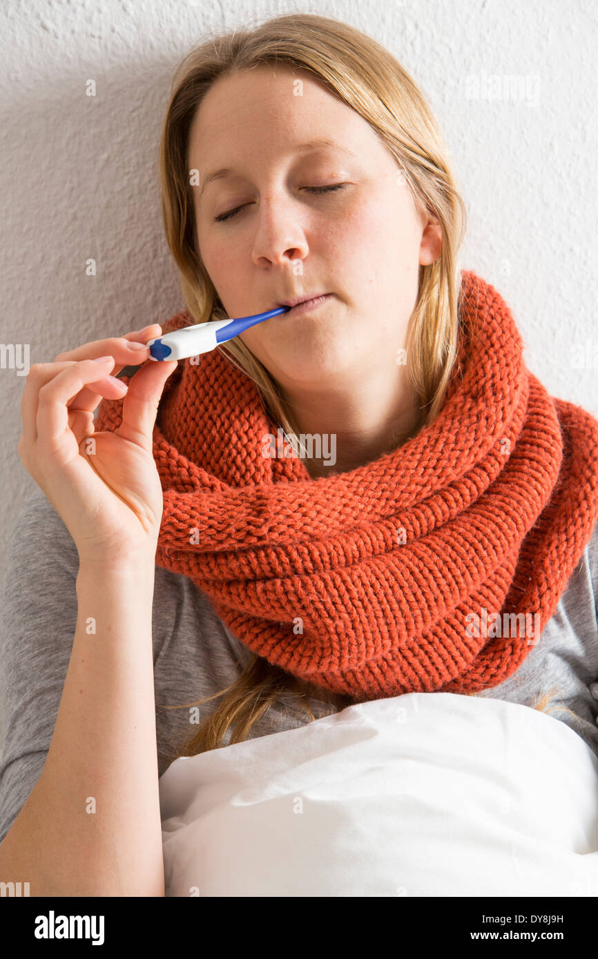 Young woman lying in bed, has a cold, fever, flu, fever, measured with