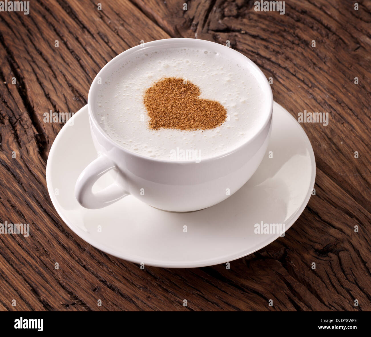 Cup of cappuccino with ground cinnamon in the form of heart on old wooden table. Top view. Stock Photo