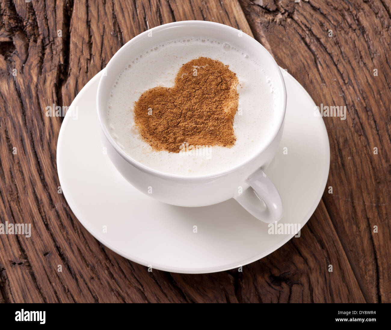 Cup of cappuccino with ground cinnamon in the form of heart on old wooden table. Top view. Stock Photo