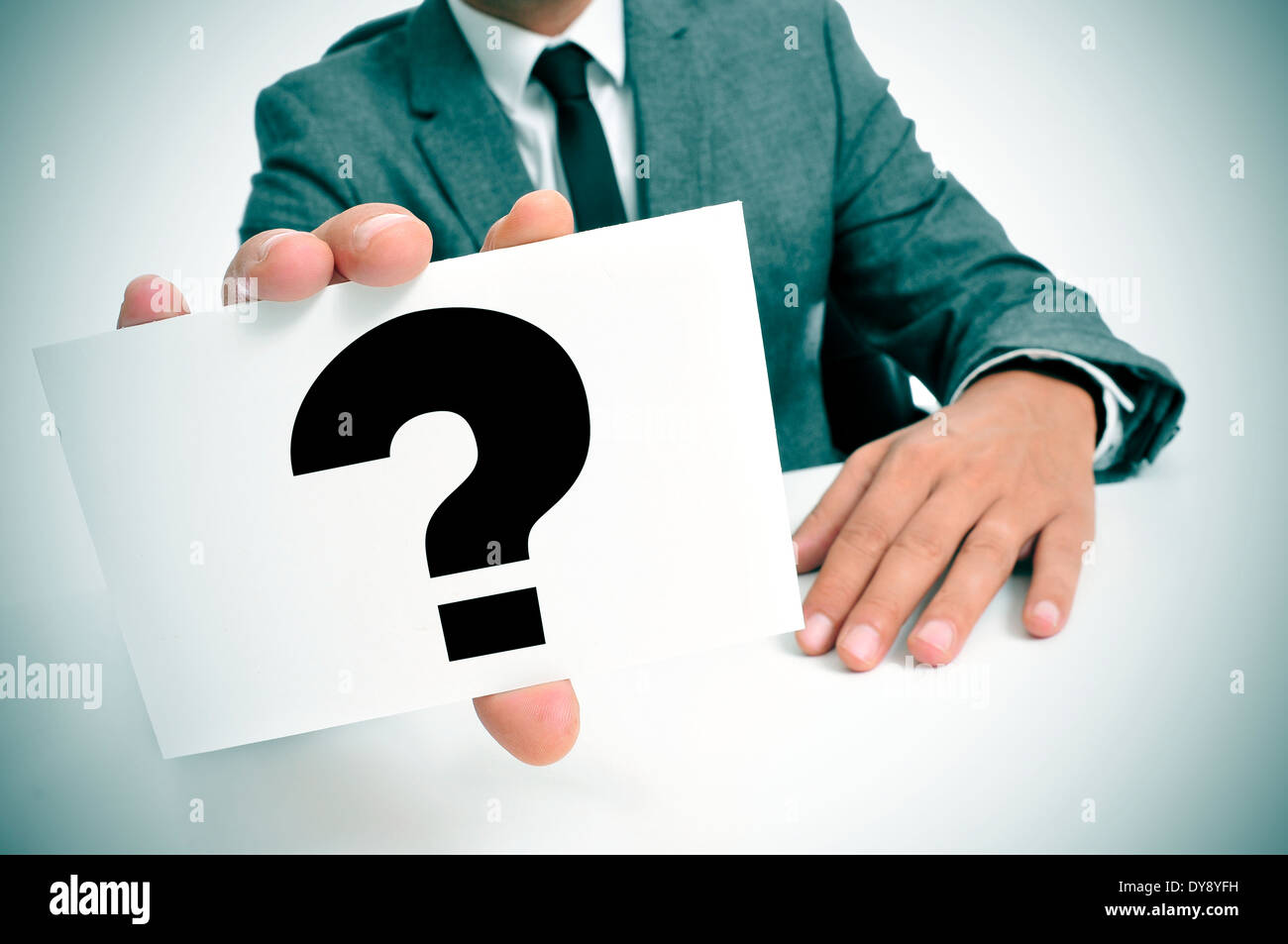 a man wearing a suit sitting in a desk holding a signboard with a question mark Stock Photo