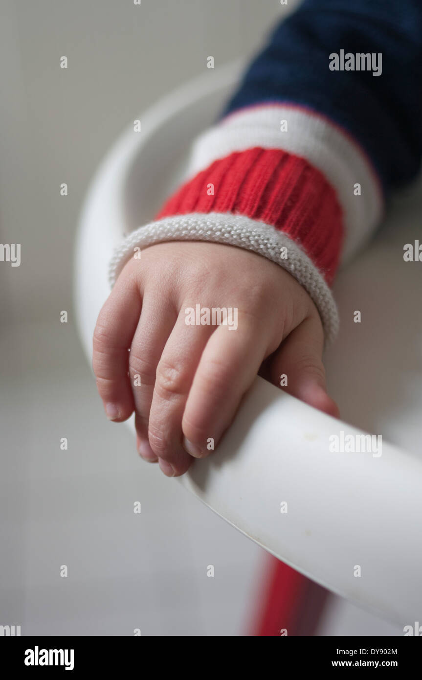 Hand of toddler holding edge of baby high chair Stock Photo