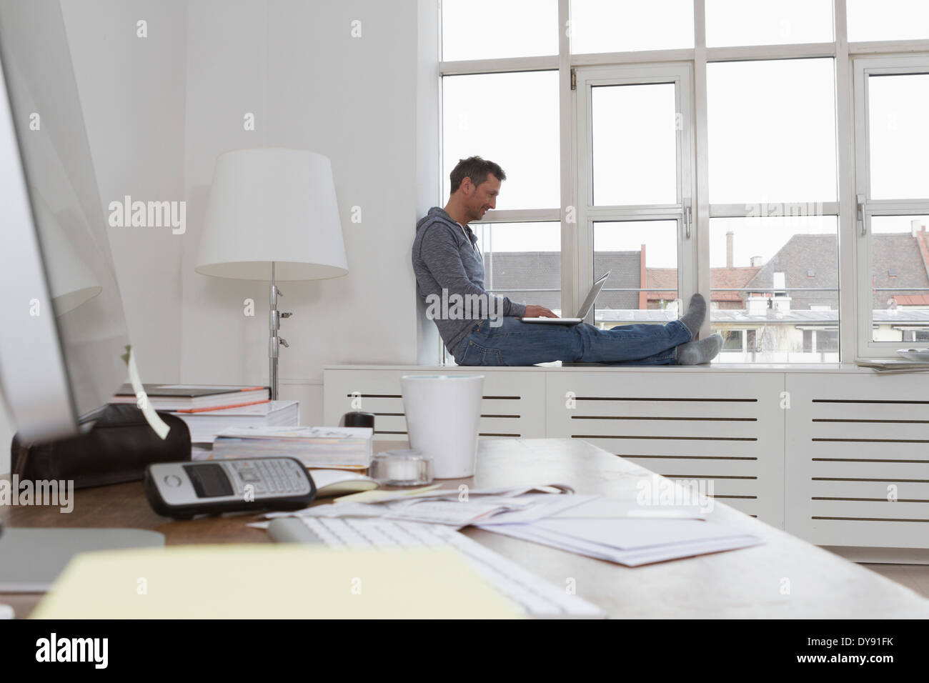 Man sitting on windowsill using laptop Stock Photo