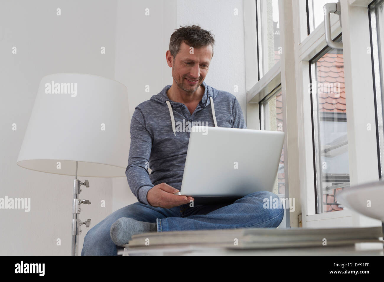 Man sitting on windowsill using laptop Stock Photo - Alamy