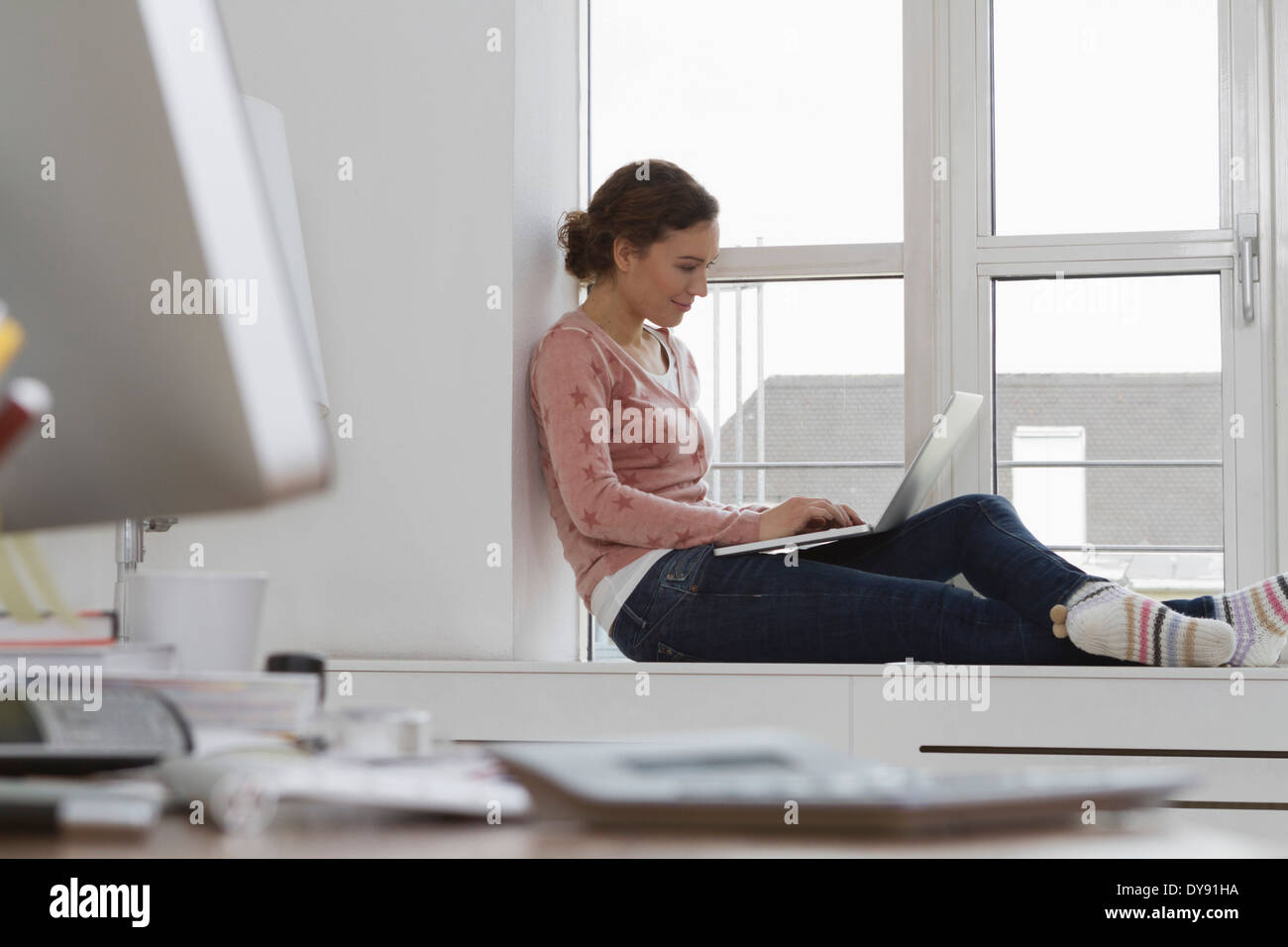 Woman sitting on windowsill using laptop Stock Photo