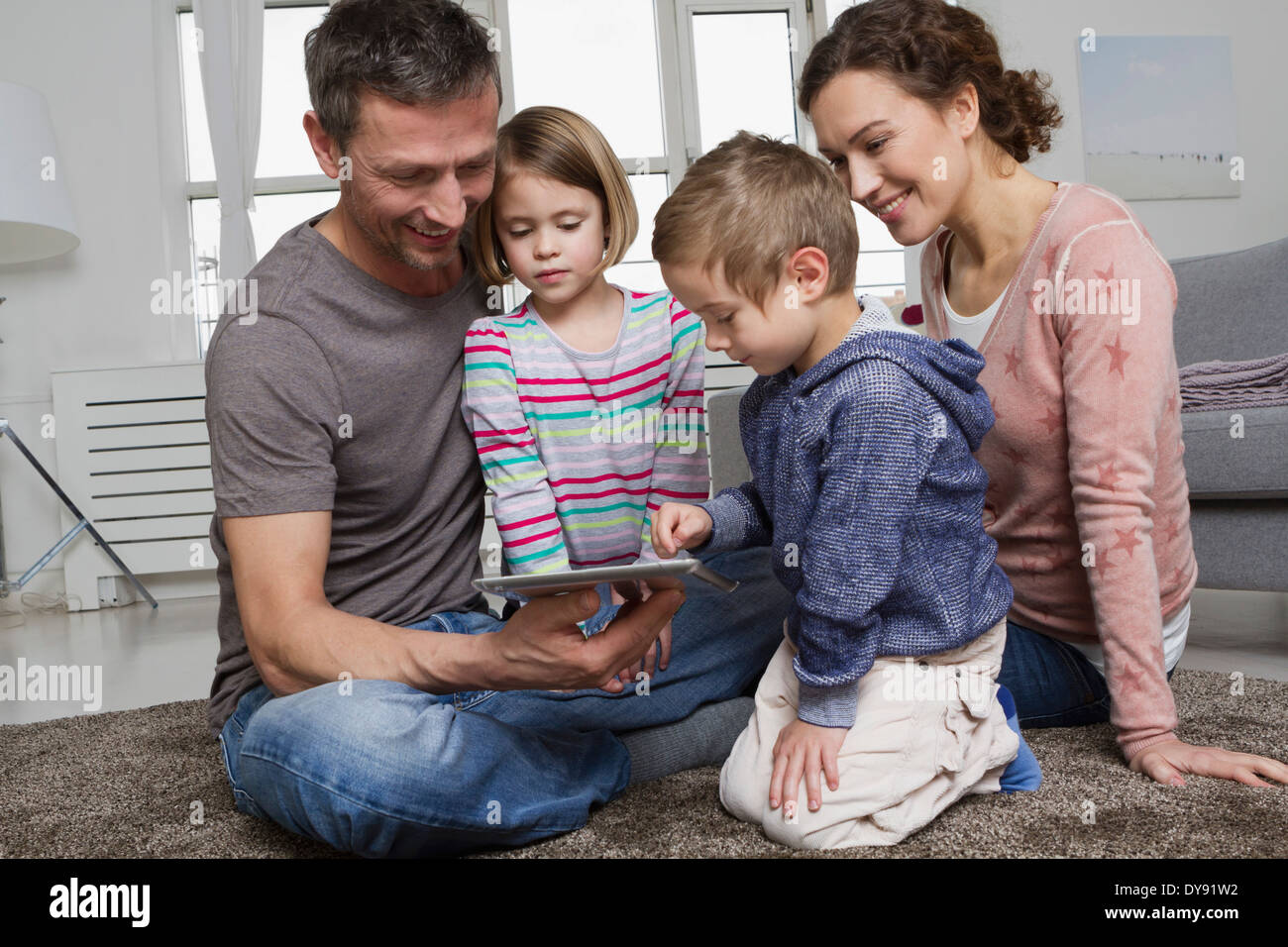 Happy family of four using tablet computer in living room Stock Photo