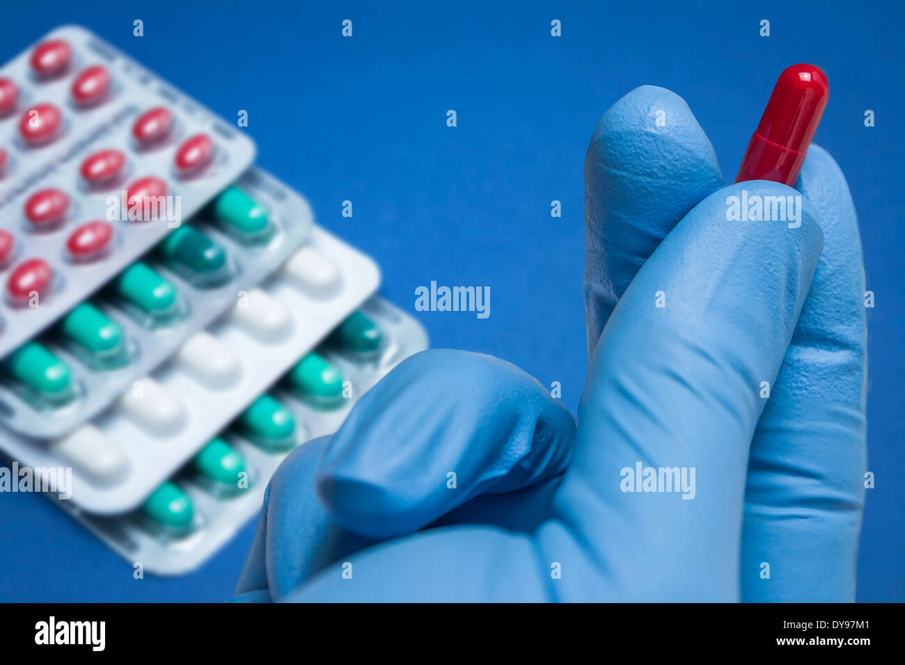 Hand with blue latex glove holds a red capsule Stock Photo