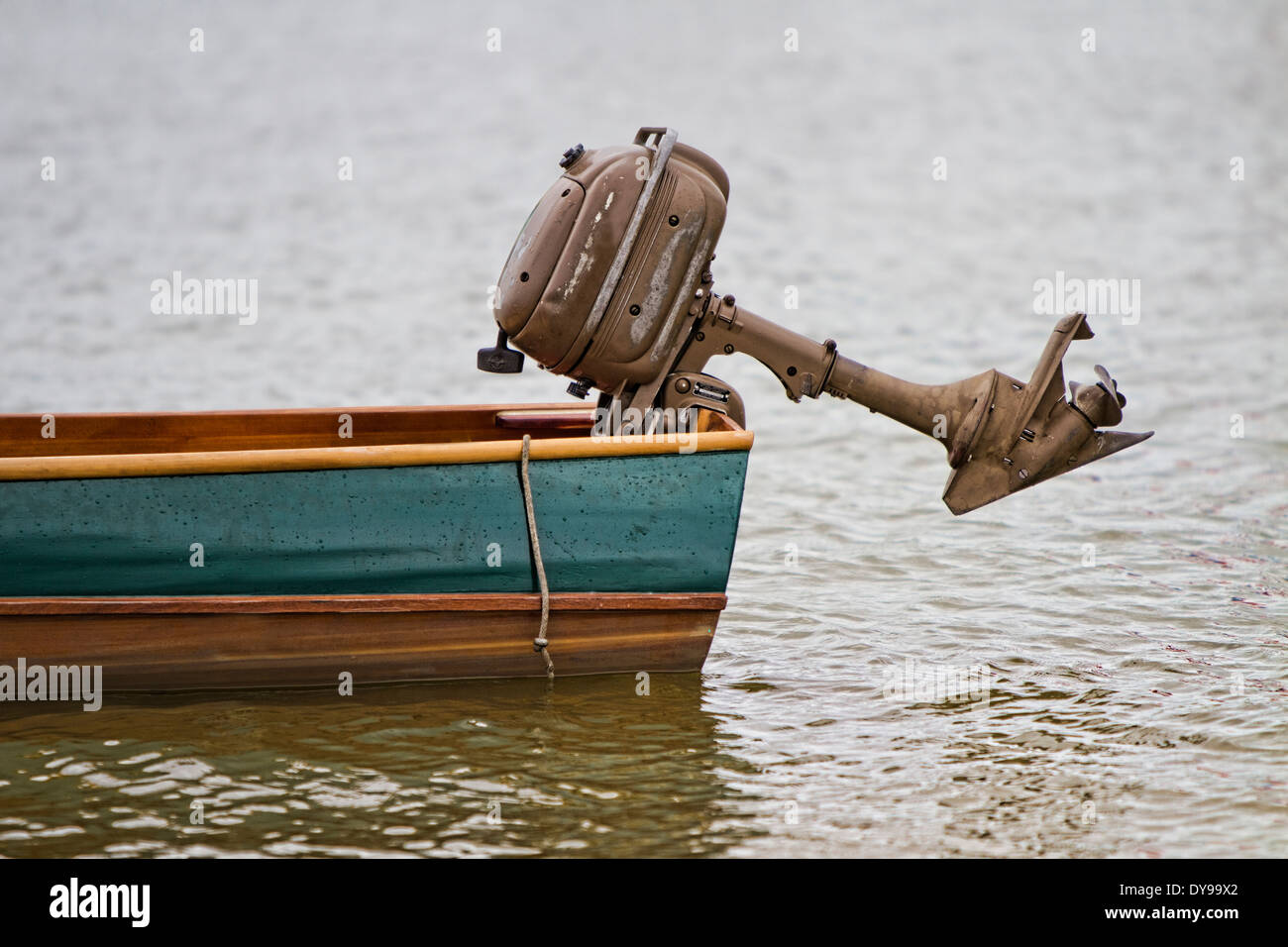 Antique Outboard Motor mounted on the transom of a wooden boat that is floating in the water Stock Photo