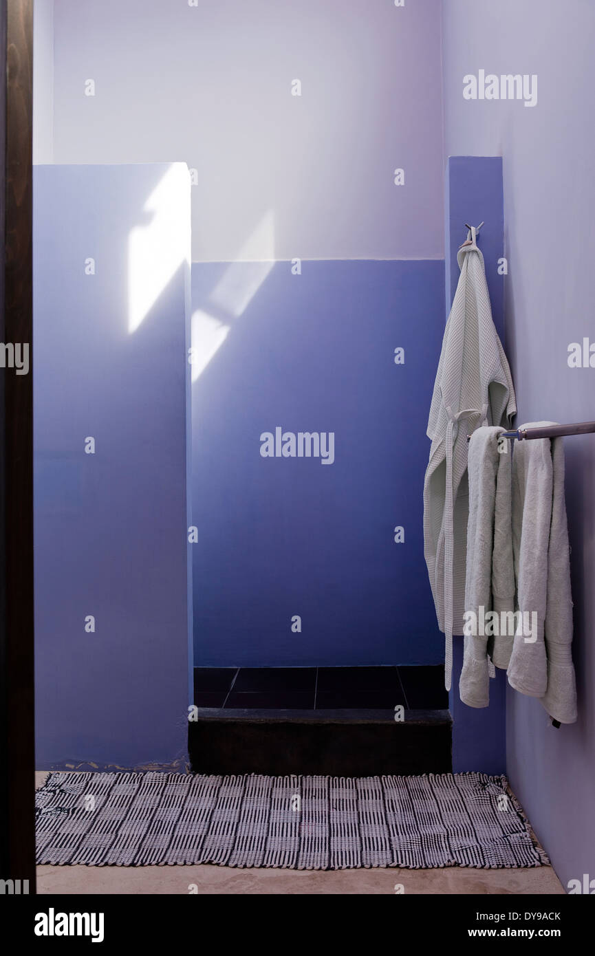 Stone shower cubicle painted in a lilac hue with black and white mexican floor mat Stock Photo