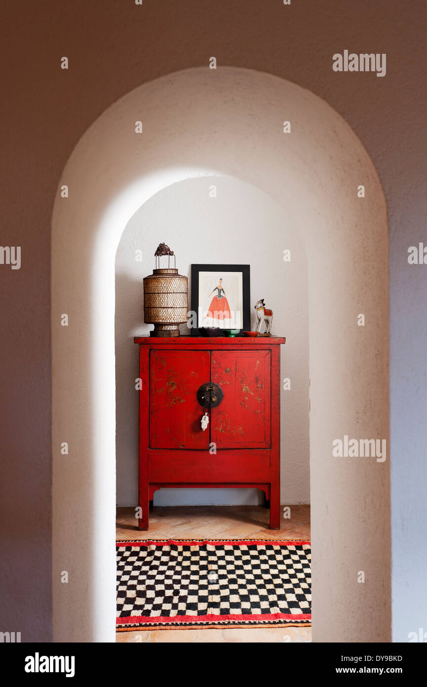 View through arched hallway to corridor with chinese red lacquer cupboard and checked runner Stock Photo