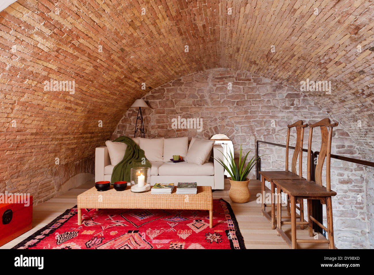 Vaulted stone walls in mezzanine space with white sofa bed, wicker coffee table and bright red ethnic rug Stock Photo