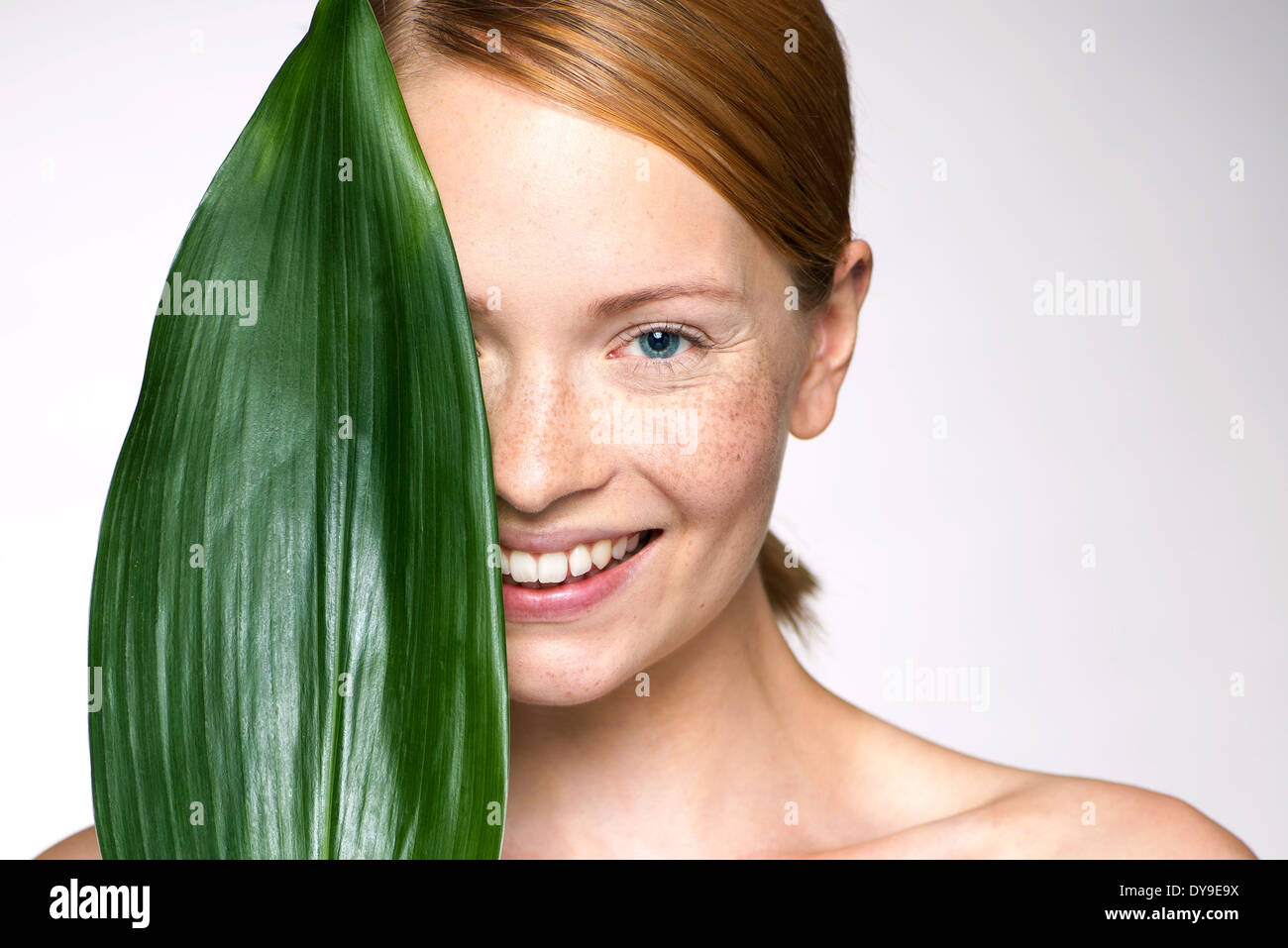 Young woman holding up leaf concealing part of face Stock Photo