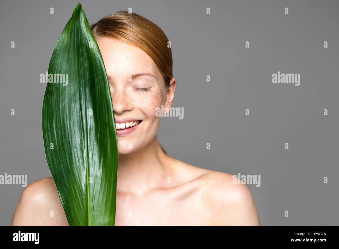 Young woman holding up leaf concealing part of face Stock Photo