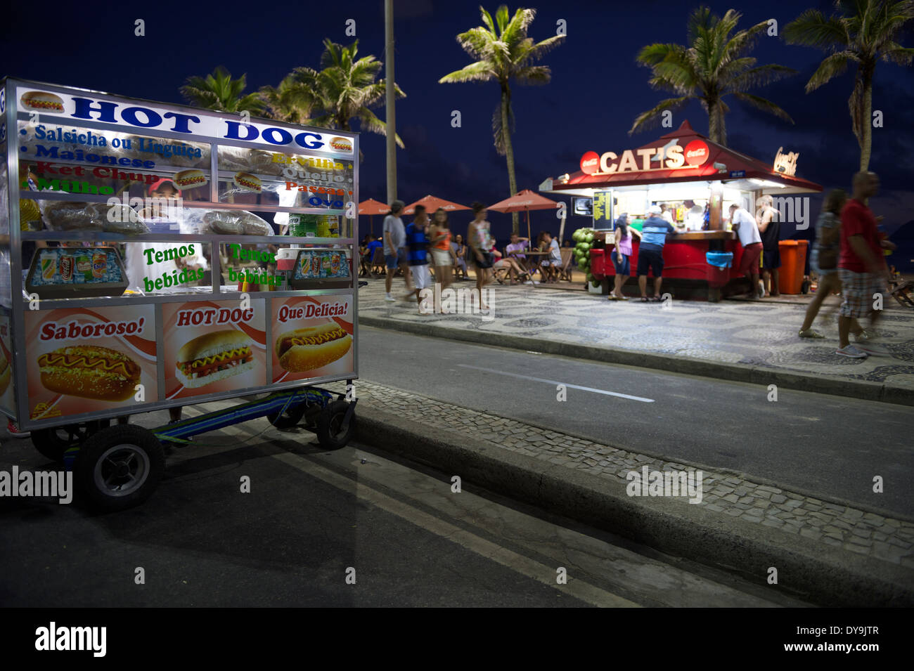 RIO DE JANEIRO, BRAZIL - JANUARY 19, 2014: Pedestriands pass a mobile hot dog stand in front of beach kiosk in a typical scene Stock Photo